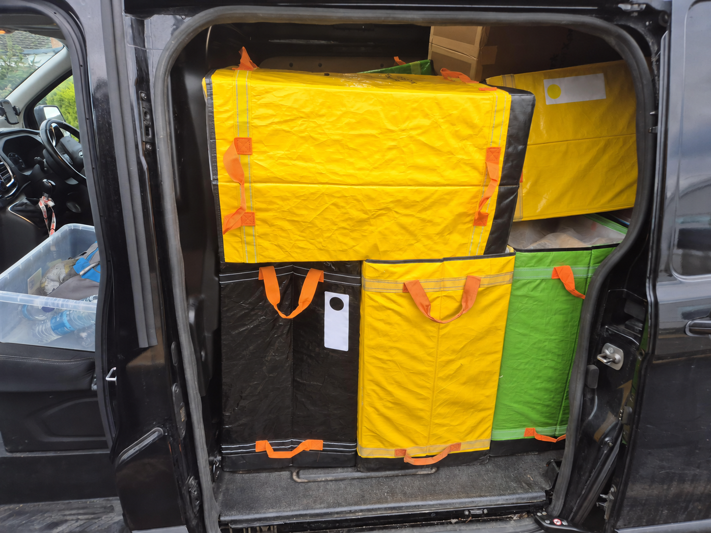 Yellow, green and black delivery bags stacked inside a van.